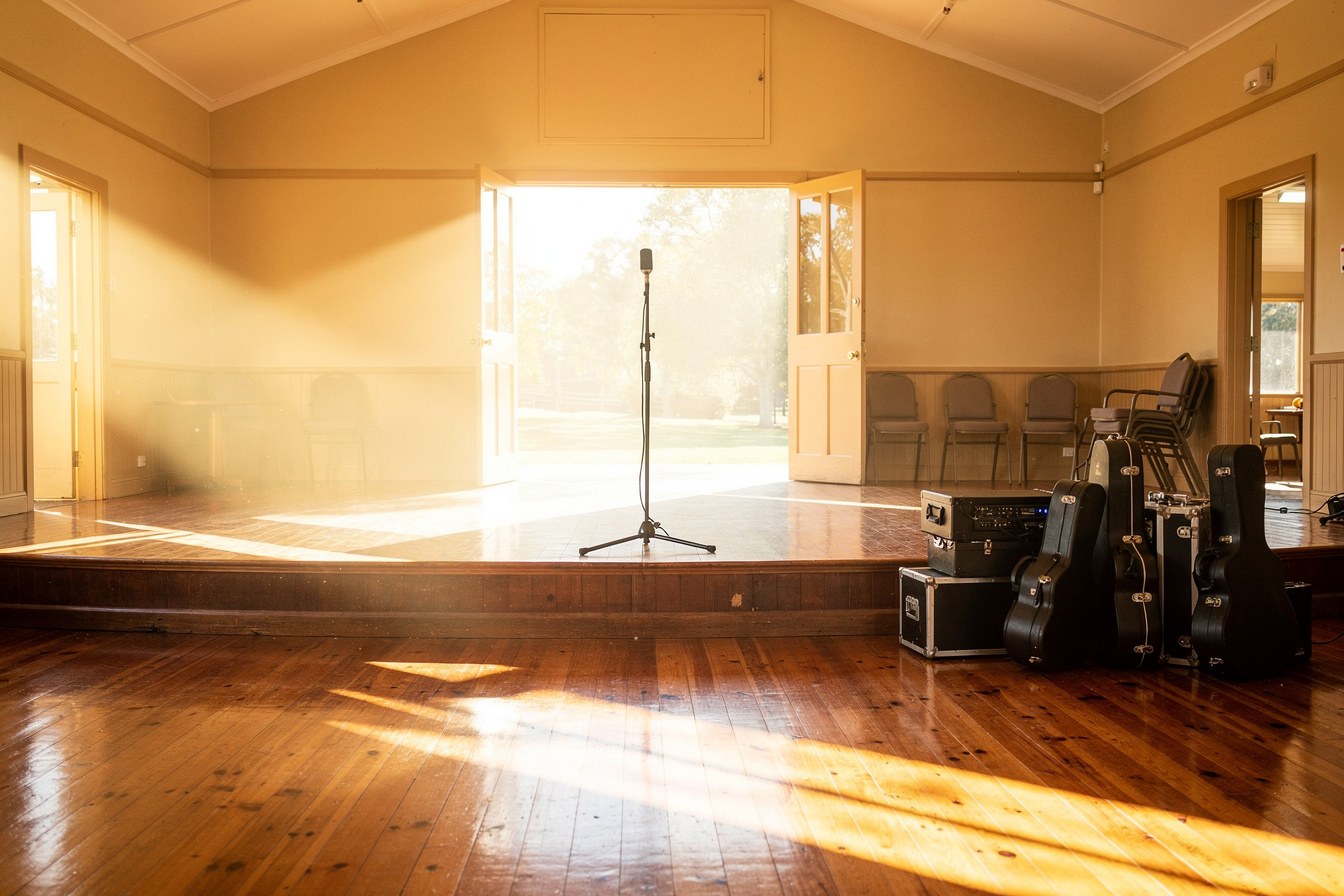 An empty regional stage with a single microphone stand, sunlight streaming through open venue doors.