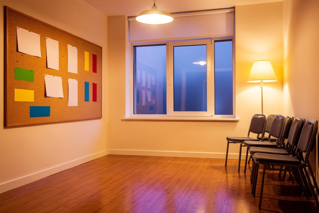 An empty community hall meeting room lit by a single warm lamp at night, evoking the late hours spent finishing a grant application after everyone else has gone home.