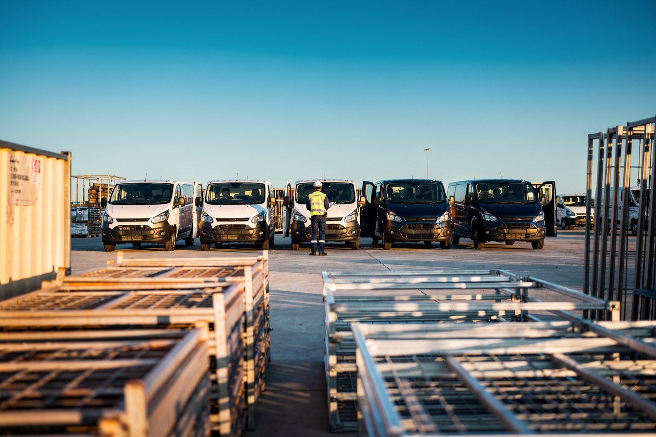 Helm Tender graphic. Headline: Register before the tender exists. Head packages are awarded. The supply chain work still needs your profile. Photo: Photorealistic editorial photograph, wide confident view of an Australian commercial vehicle and equipment supply yard bathed in radiant morning light:…