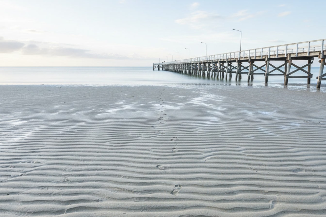A tide line pattern on sand at a Queensland jetty, suggesting reading recurring signals before they arrive.